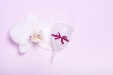 Eco-friendly silicone menstrual cup with orchid on pink background.
