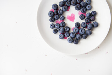 Delicious blueberries lie on a plate with a heart inside. Delicious and healthy food. Place for an inscription.