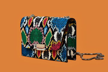 Close-up of a fashionable small handbag, a snakeskin clutch in bright colors. A fashion accessory. Orange isolated background.