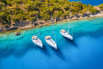 Fototapeta na wymiar Aerial view of beautiful yachts and boats on the sea at sunset in summer. Gemiler Island in Turkey. Top view of luxury yachts, sailboats, clear blue water, beach, mountain and green trees. Travel