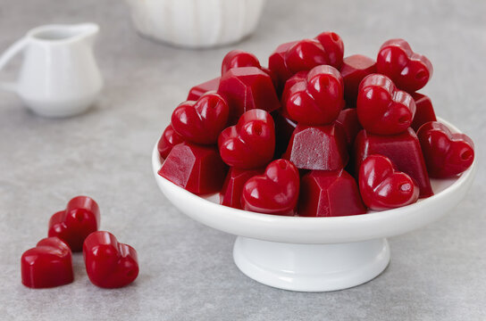 Homemade Gummy Candy. Red Heart shaped jelly sweets served on white serving stand with syrup pitcher on background. 
