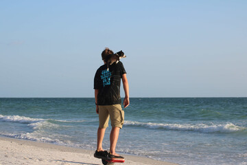Young man on hover board with dog on shoulder on beach