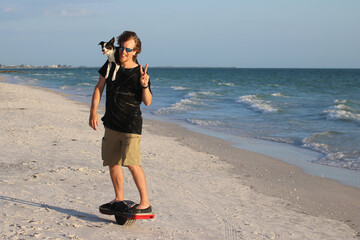 Young man on hover board with dog on shoulder on beach