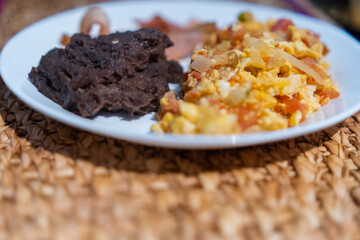 Mexican-style eggs, bacon, and refried beans on a white plate