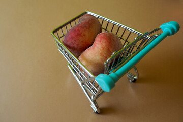 close-up two whole figs pink peaches lie in a mini trolley from a supermarket on a brown...