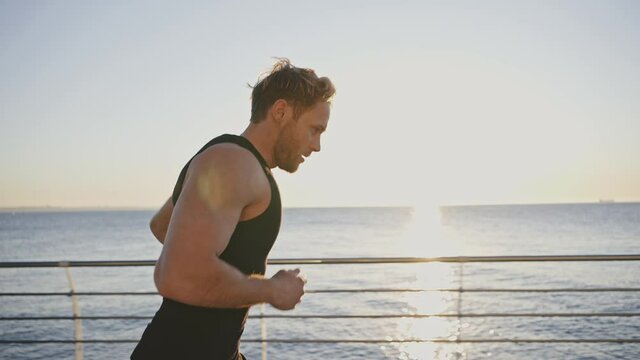 Healthy lifestyle and sports habits. Close up follow shot of sporty man sprinter running at seaside early in morning