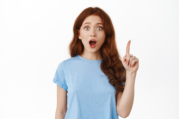 Got an idea. Excited redhead woman raising finger and gasping, have great plan, saying suggestion, standing in t-shirt against white background