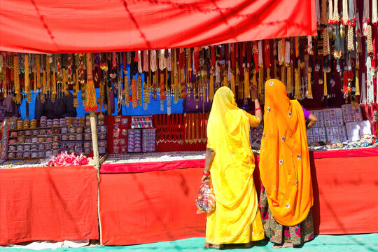 Couple of unidentified women in traditional hindu wear saree buying or shopping jewelery items in the commercial street of Pushkar fair in state of Rajasthan, India. Colorful Indian culture concept