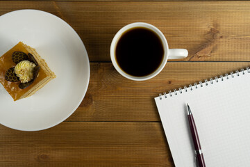 Top view of coffee cup, cake on the plate and blank notebook with pen on wooden table.