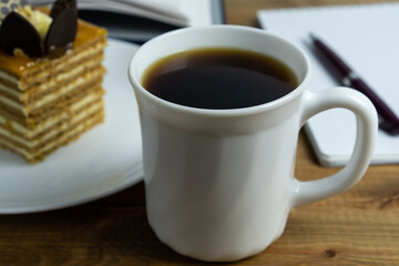 Cup of coffee close up and cake on the plate on wooden table. Concept coffee break and relaxation.