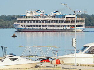 A river theme. A pier with boats on foreground and three-deck passenger cruise ship on background....