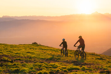 Mother and daughter cycling uphill with mountain bikes at a sunset.