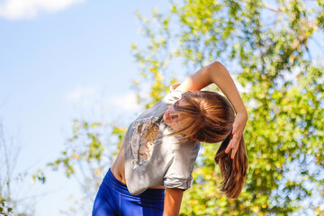 Obraz premium Defocus caucasian preteen girl doing physical exercise in park, forest, outdoor, outside. Meditation, concentration. Healthy lifestyle. Side bend exercise. Green background. Out of focus