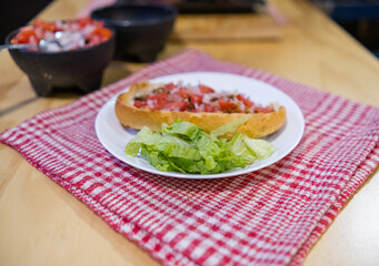 Mexican mollete and lettuce on a plate above white and red checkered napkin