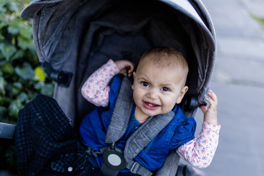 Adorably and concerned-looking baby in a gray stroller on the sidewalk