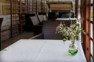 Interior of a summer cafe: table covered with tablecloth and white tender flowers in a glass vase on it