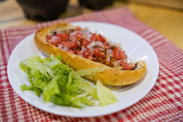Mexican mollete and lettuce on a plate above white and red checkered napkin
