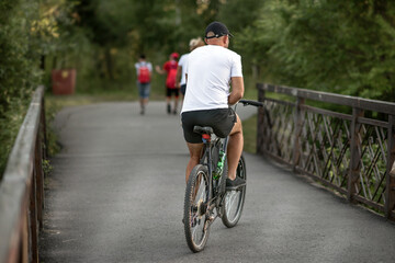 A young man riding a bicycle in a park on a bridge in summer in the morning.