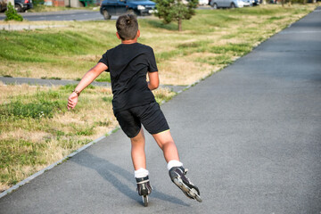 A sporting, athletic boy roller skating in a park on a summer day.