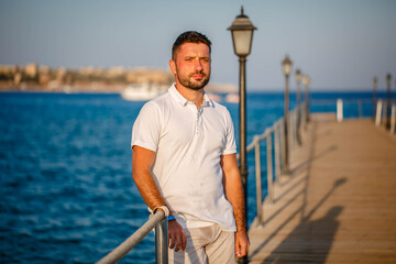 Tourist man in white t-shirt on the sea pier enjoying the sunset