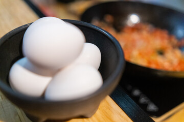 Eggs in small black bowl with blurry food in pan as background