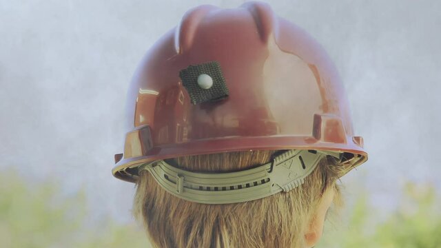 Young Boy Wearing Hard Hat around Cigarette Smoke Outdoors. Back View. Close Up. 4K Resolution.