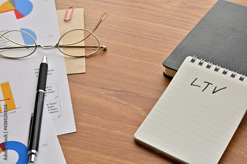 Poster there is a note book with the word of ltv. it's on the desk with a laptop, a pen and papers of dummy