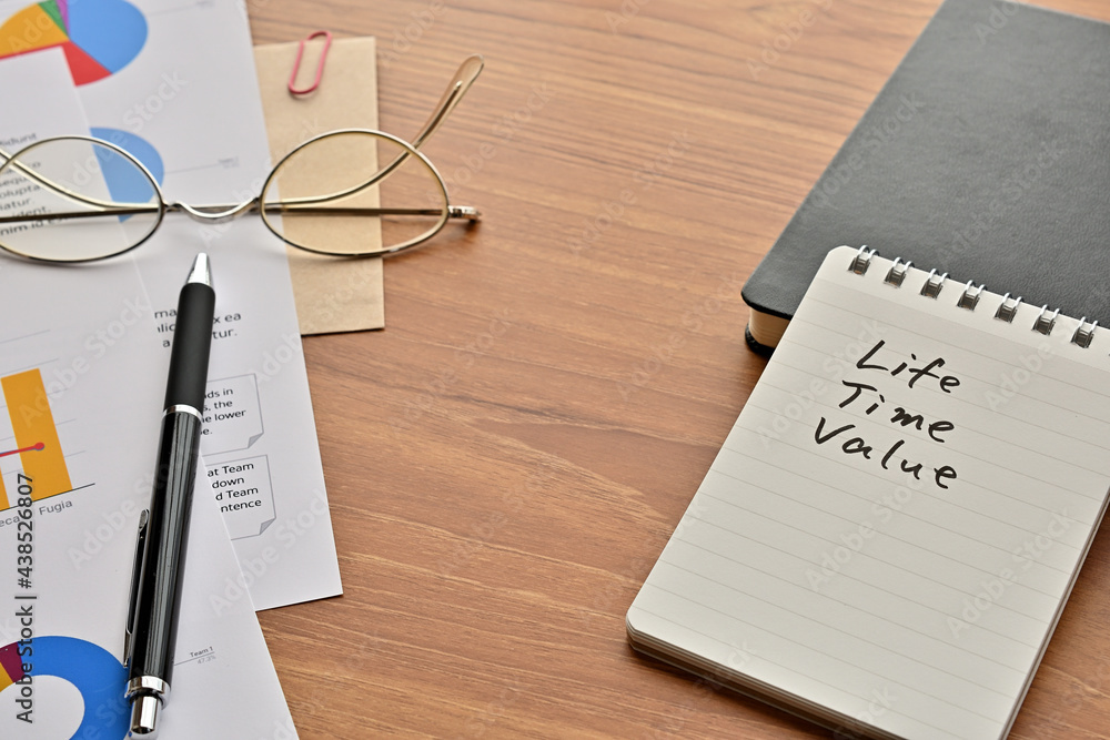 Poster there is a note book with the word of life time value. it's on the desk with a laptop, a pen and pap