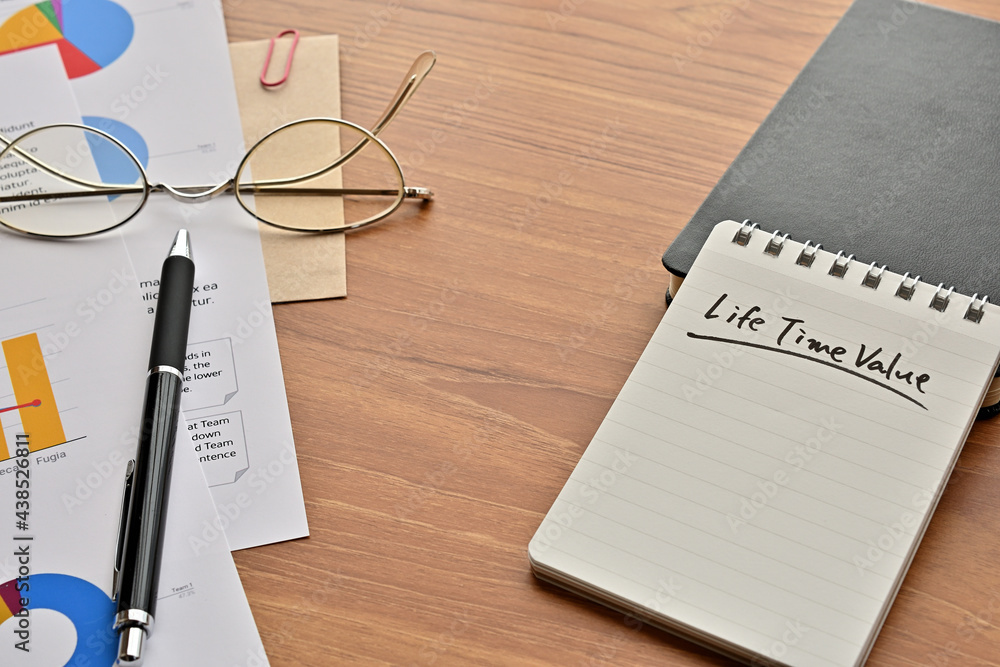 Poster there is a note book with the word of life time value. it's on the desk with a laptop, a pen and pap