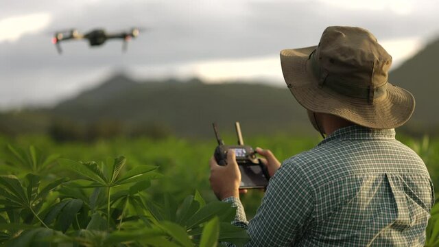 Asian farmer using drone flying navigating above farmland with beautiful sunrise. A young farmer controls a drone in a large scale survey of agricultural plots for modern farming and farming.