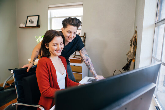 Lesbian woman showing her wife something on computer in home office