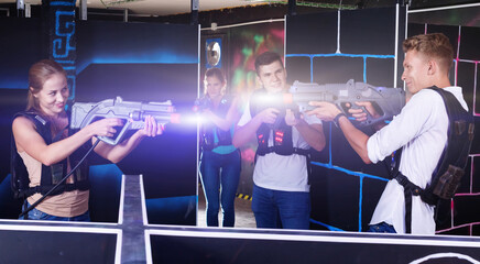 Fototapeta na wymiar Laser tag players happy positive smiling guys and girls playing in teams in dark laser tag room
