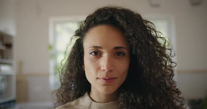 Portrait of a beautiful multi ethnic woman with curly hair slightly smiling and looking to the camera. Close up, slow motion. 