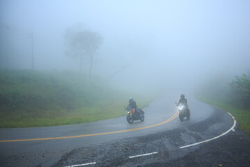 Two people riding a motorbike on foggy road in morning