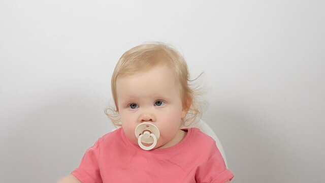 Portrait of cute funny little blonde child posing with pacifier in mouth sitting in feeding chair