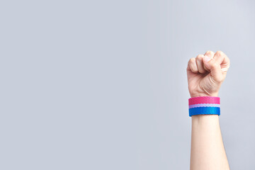 Raised fist of a person wearing a bracelet with the colors of the bisexual flag