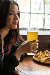 beautiful person smiling with long hair, holding a plate of nachos while holding a glass with a...