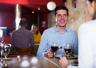 Positive man with girlfriend enjoying evening meal at cozy restaurant
