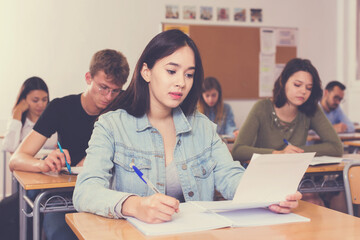 Obraz premium Young female student is learning and answering the question on paper in the class