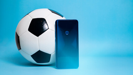 Smartphone next to soccer ball on blue background 