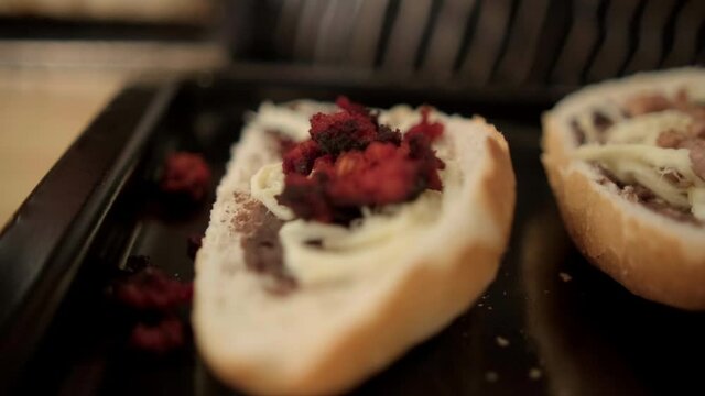 Blue tongs adding chopped meat to traditional Mexican molletes above black tray