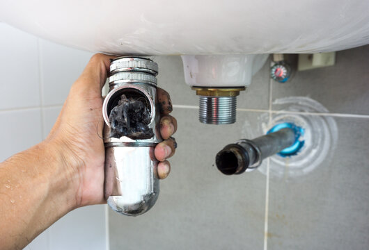 Hand of Plumber holding joints and connections of Basin or sink in a bathroom, Clearing a Clogged Bathroom Sink in a bathroom for unclog a Sink.