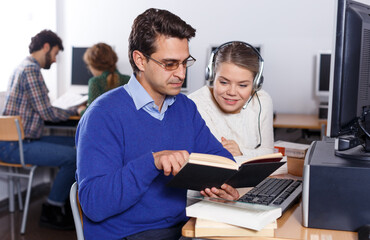 Obraz premium Intelligent female and male students working together with computer and book in university library ..