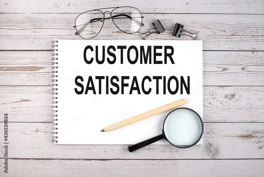 Poster notebook with text customer satisfaction on the wooden table with pen, magnifier and glasses