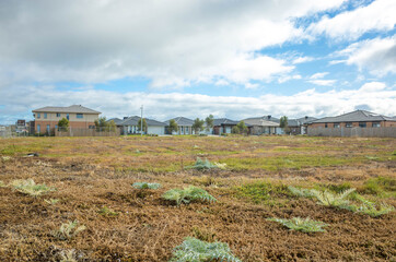 Fenced vacant land near some Australian new residential suburban houses. Concept of real estate development, housing, land for sale and a new suburb, Tarneit, Melbourne, VIC Australia.
