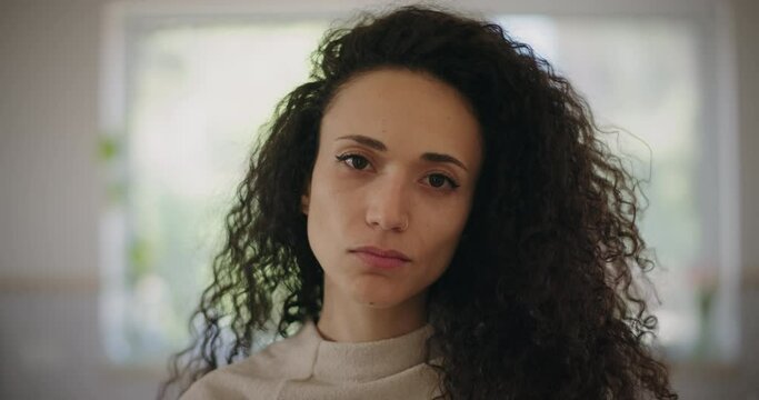Portrait of a sad young woman with curly hair looking at the camera. Close up, slow motion. 