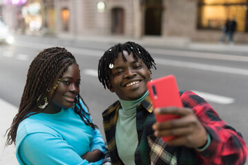 Smiling black couple taking a selfie on the street.