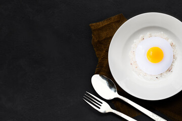 Fried egg with rice white plate and spoon, fork empty on dark stone table background