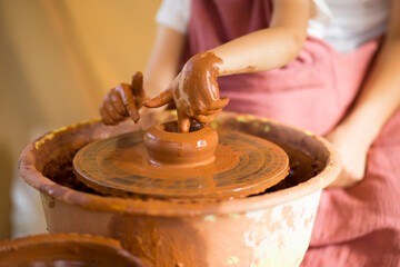 Fototapeta premium Master class for the child. Teacher hands show to kid how make ceramics dishes on potter wheel. Artist works with clay. Little girl sculpt cup clay