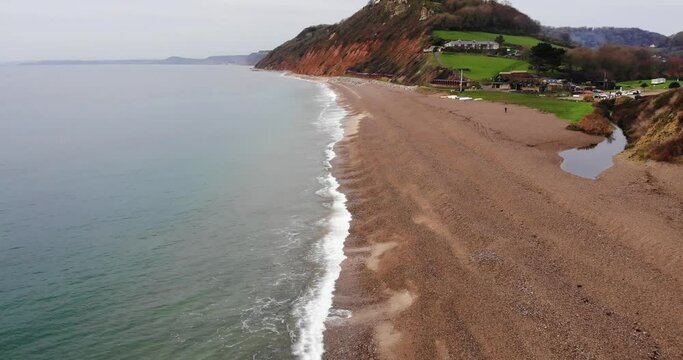 4K Smooth Aerial shot skirting above the oceans edge and glimpsing the mountains and rolling hills of Branscombe Beach